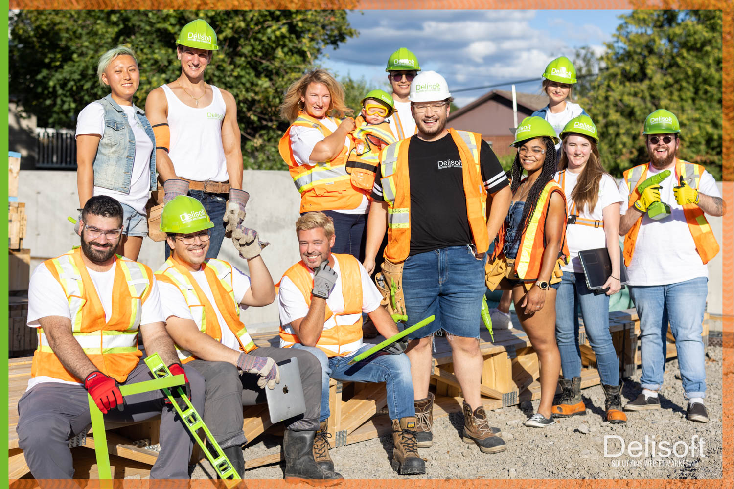 Équipe Delisoft sur un chantier de construction, portant des casques verts et des gilets de sécurité orange, souriant et posant avec divers outils de construction.